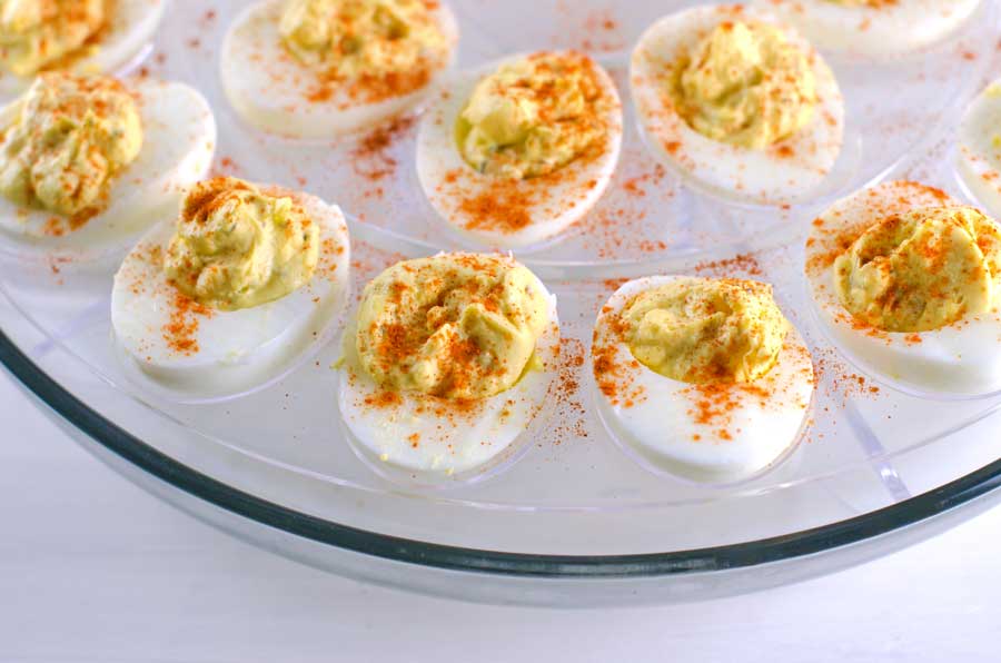 Closeup of prepared deviled eggs in a glass deviled egg tray on a white wood surface