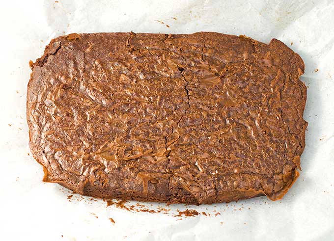 A 9 x 13 slab of baked brownies sitting on parchment paper while cooling.