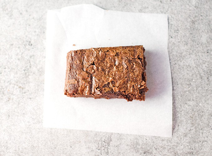 A baked and sliced brownie sitting on a white square of parchment paper on a light gray background.