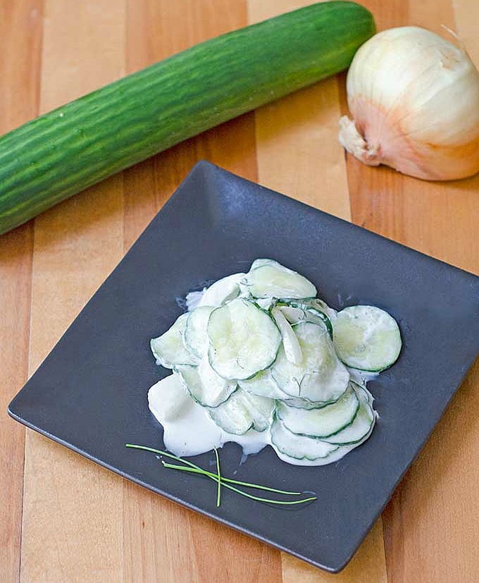 Prepared creamy cucumber salad black square plate garnished with fresh chives.
