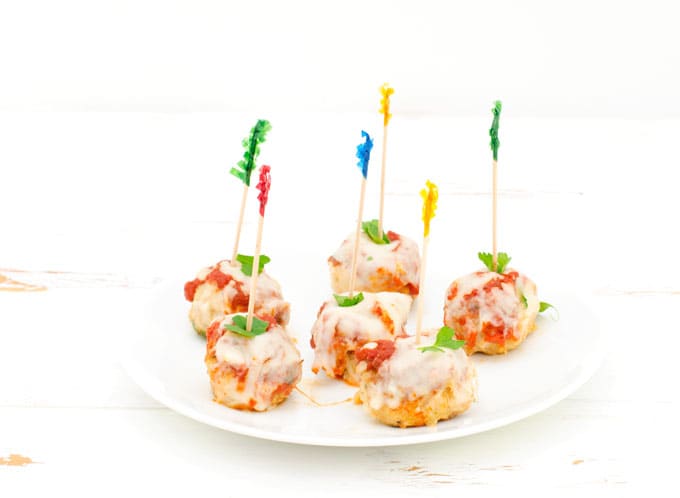 Prepared chicken parmesan meatballs on a small white plate with a toothpick for easy eating