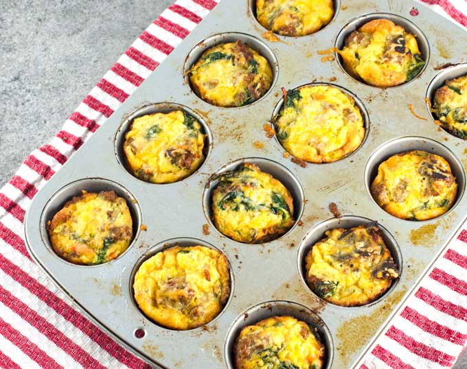 baked frittatas cooling in the muffin tin on a white and red striped towel on a dark gray surface