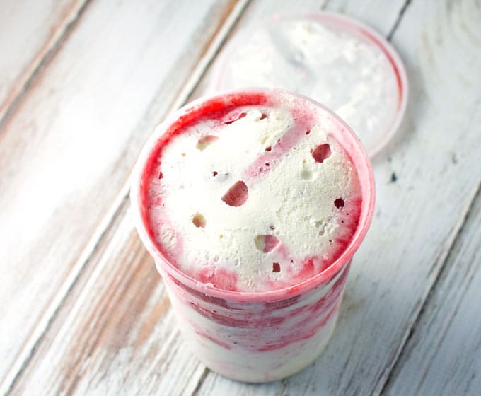frozen strawberry swirl ice cream in a clear pint container on a brown and white distressed table top