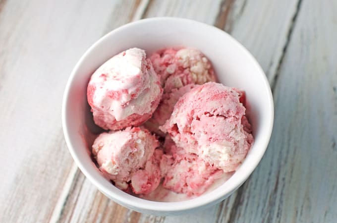 no-churn strawberry ice cream scooped into a white bowl on a brown and white distressed table top